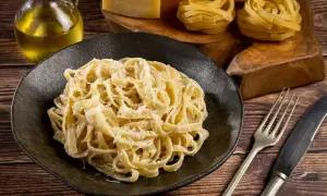 Pyszne fettuccine alfredo na czarnym talerzu, obok surowy makaron, ser i oliwa.