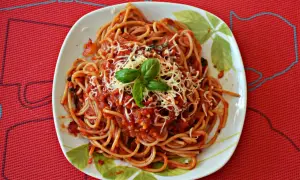 Pyszne spaghetti napoli z sosem pomidorowym, startym serem i listkami bazylii na talerzu.