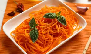Pyszna surówka z marchewki, udekorowana listkami bazylii, obok czosnku i papryczek chili.