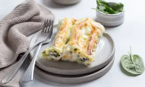 Pyszne cannelloni ze szpinakiem, zapieczone pod beszamelem i serem, na talerzu z widelcem i serwetką.