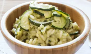 Kremowe risotto z cukinią, podane w drewnianej misce, ozdobione plasterkami zielonej cukinii.