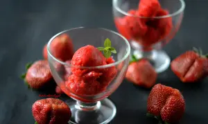 Orzeźwiający sorbet truskawkowy w pucharkach, otoczony świeżymi truskawkami. Idealny na upalne dni.