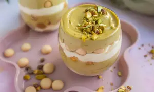 Pyszne tiramisu pistacjowe w szklance, przełożone kremem i biszkoptami, posypane orzechami pistacjowymi.
