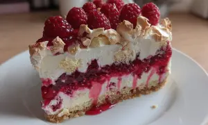 Pyszny deser z warstwami kremu, biszkoptu i intensywną frużeliną malinową, zwieńczony świeżymi malinami i bezą.