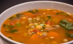 Aromaticzna zupa z ciecierzycy z kawałkami pomidorów, marchewki i świeżą kolendrą.