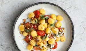 Pyszne gnocchi z sosem pomidorowym, listkami szałwii i orzechami na talerzu.