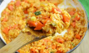 Kremowe risotto pomidorowe z kawałkami marchewki i cukinii, nabierane drewnianą łyżką.