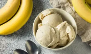 Pyszne lody bananowe w miseczce, obok świeże banany i łyżeczki. Idealne na upalne dni.