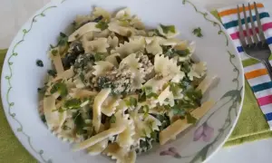 Pyszny makaron farfalle z tuńczykiem i zielonymi ziołami, podany na talerzu z ozdobnym brzegiem.