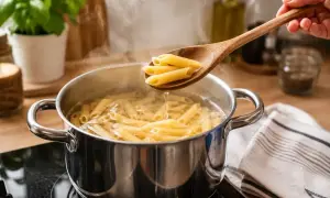Gotowy przepis na makaron: penne gotuje się w garnku, a drewniana łyżka wyciąga porcję.