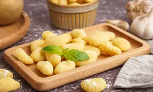 Pyszne, domowe gnocchi na drewnianej desce. Idealny przepis na obiad. W tle czosnek i ziemniaki.