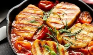 Pyszne halloumi z piekarnika w sosie pomidorowym z ziołami, podane w żeliwnej patelni.
