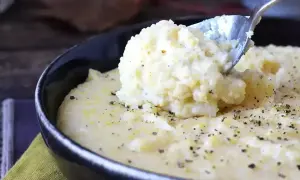 Kremowa polenta, idealna do prostego przepisu. Łyżka wydobywa porcję tej pysznej potrawy, posypanej pieprzem.