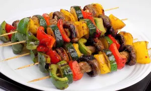 Kolorowe szaszłyki warzywne z papryką, cukinią i pieczarkami, grillowane do perfekcji, prezentują się apetycznie na białym talerzu.