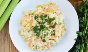 Kremowe risotto z krewetkami, posypane świeżą natką pietruszki, obok łodygi selera i oliwy.