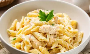 Pyszny makaron penne w kremowym sosie z kawałkami kurczaka, udekorowany natką pietruszki. Idealny na szybki obiad.