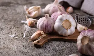 Główki czosnku na desce, obok praska. Idealne do suszenia i dodawania smaku potrawom.