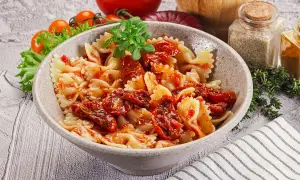 Pyszny makaron farfalle z aromatycznymi suszonymi pomidorami, udekorowany świeżą bazylią.