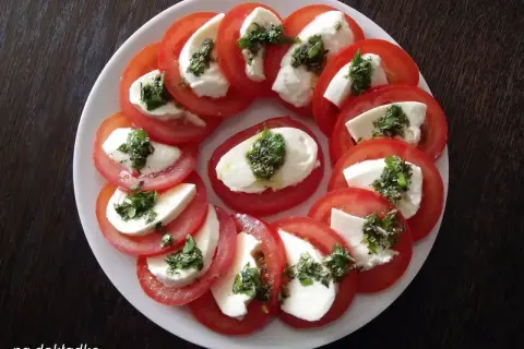 Pyszne pomidory z mozzarellą, ułożone na talerzu, posypane ziołami. Idealna przekąska na lato.