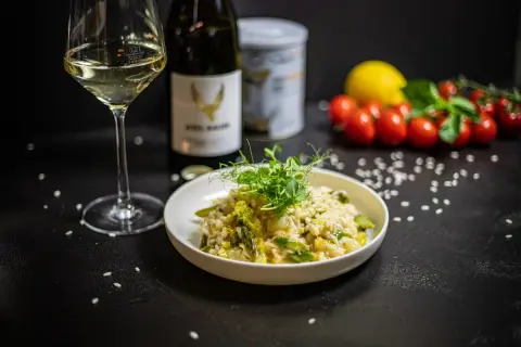 Aksamitne risotto z kurczakiem i szparagami, udekorowane kiełkami. Obok kieliszek białego wina i butelka.
