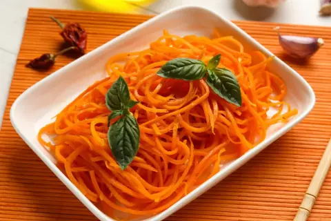 Pyszna surówka z marchewki, udekorowana listkami bazylii, obok czosnku i papryczek chili.