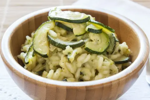 Kremowe risotto z cukinią, podane w drewnianej misce, ozdobione plasterkami zielonej cukinii.