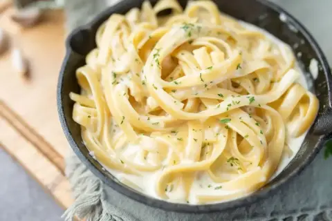 Pyszny makaron fettuccine w kremowym sosie, posypany natką pietruszki. Idealny pomysł, z czym zrobić makaron na szybko.