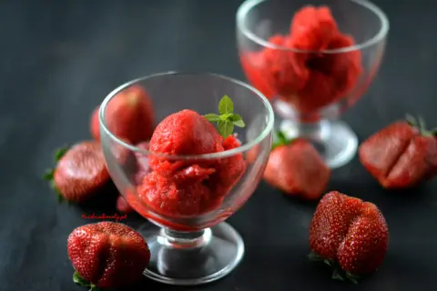 Orzeźwiający sorbet truskawkowy w pucharkach, otoczony świeżymi truskawkami. Idealny na upalne dni.