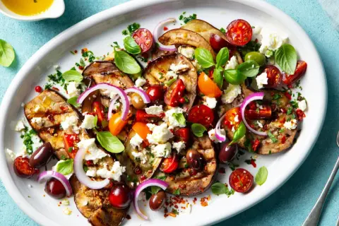 Pyszna sałatka z grillowanych warzyw: bakłażan, pomidorki, oliwki, cebula i ser feta, skropiona oliwą.