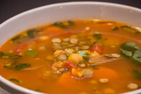 Aromaticzna zupa z ciecierzycy z kawałkami pomidorów, marchewki i świeżą kolendrą.