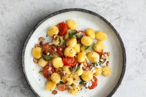 Pyszne gnocchi z sosem pomidorowym, listkami szałwii i orzechami na talerzu.