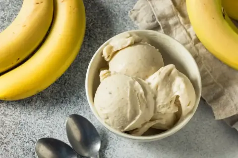 Pyszne lody bananowe w miseczce, obok świeże banany i łyżeczki. Idealne na upalne dni.