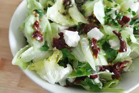 Chrupiąca sałata lodowa z serem feta, suszonymi pomidorami i pestkami dyni. Pyszna i lekka sałatka.