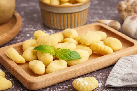 Pyszne, domowe gnocchi na drewnianej desce. Idealny przepis na obiad. W tle czosnek i ziemniaki.
