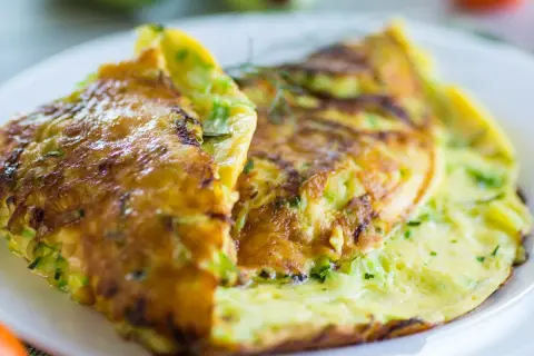 Złocisty omlet z cukinią, delikatnie zrumieniony, podany na białym talerzu. Pyszne śniadanie pełne warzyw.