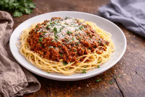 Pyszne makaron spaghetti z bogatym sosem bolońskim, posypane parmezanem i natką pietruszki.