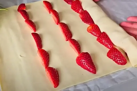 Słodkie truskawki w cieście francuskim układane w rzędach, gotowe do pieczenia.