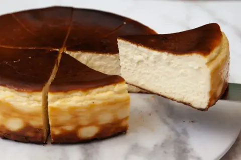 Kawałek pysznego, lekko przypieczonego basque cheesecake jest wyjmowany z całego ciasta.