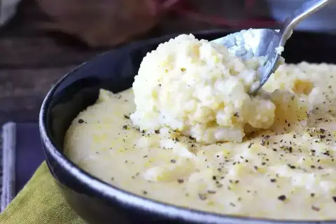Kremowa polenta, idealna do prostego przepisu. Łyżka wydobywa porcję tej pysznej potrawy, posypanej pieprzem.