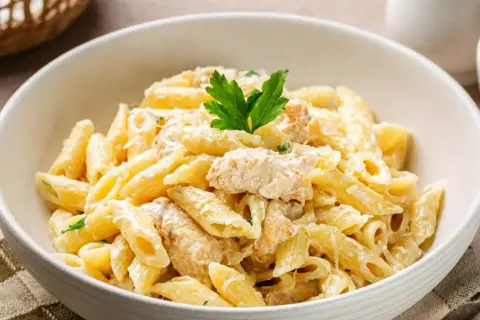 Pyszny makaron penne w kremowym sosie z kawałkami kurczaka, udekorowany natką pietruszki. Idealny na szybki obiad.
