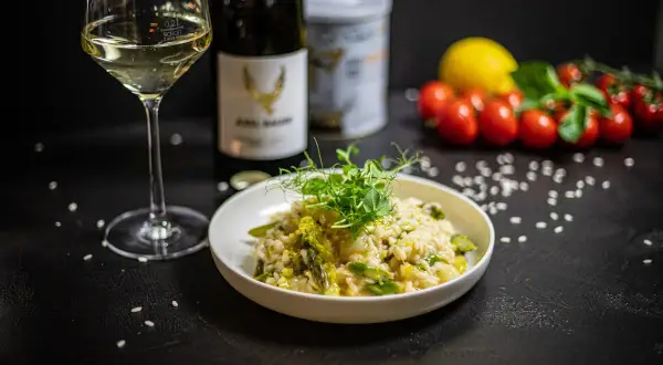 Aksamitne risotto z kurczakiem i szparagami, udekorowane kiełkami. Obok kieliszek białego wina i butelka.