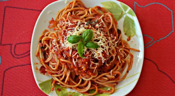 Pyszne spaghetti napoli z sosem pomidorowym, startym serem i listkami bazylii na talerzu.