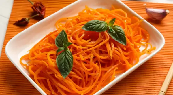 Pyszna surówka z marchewki, udekorowana listkami bazylii, obok czosnku i papryczek chili.