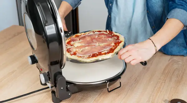 Osoba wkłada pizzę do pieca. Dowiedz się, w jakiej temperaturze piec pizzę, aby uzyskać idealny smak.