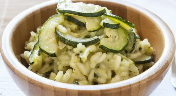 Kremowe risotto z cukinią, podane w drewnianej misce, ozdobione plasterkami zielonej cukinii.
