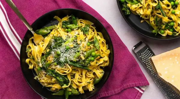 Pyszne pasta primavera z zielonymi warzywami i parmezanem, podane na talerzu.