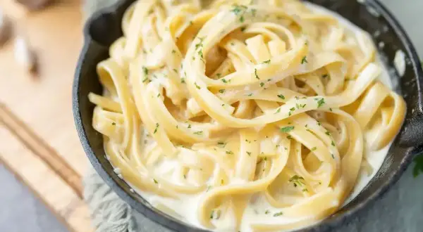 Pyszny makaron fettuccine w kremowym sosie, posypany natką pietruszki. Idealny pomysł, z czym zrobić makaron na szybko.