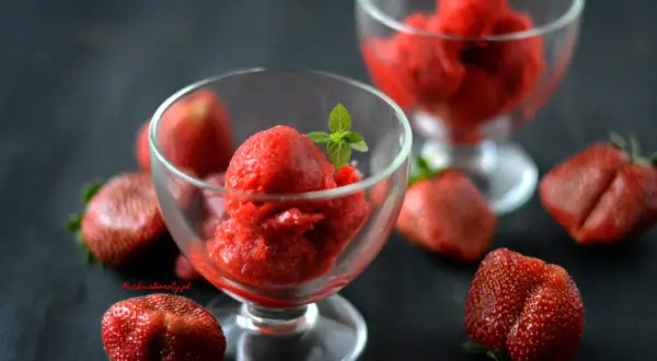 Orzeźwiający sorbet truskawkowy w pucharkach, otoczony świeżymi truskawkami. Idealny na upalne dni.