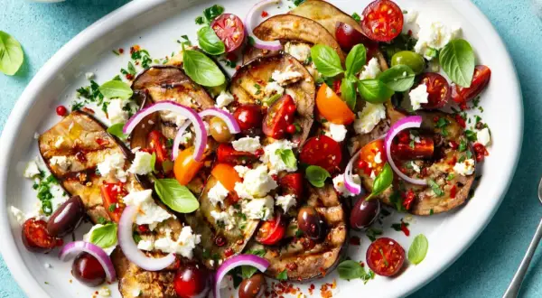 Pyszna sałatka z grillowanych warzyw: bakłażan, pomidorki, oliwki, cebula i ser feta, skropiona oliwą.