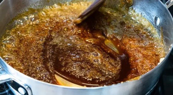 Brązowy, bulgoczący płyn w garnku, to palone masło, które nabiera głębokiego aromatu. Drewniana łyżka miesza je, tworząc karmelowe refleksy.